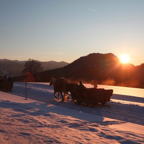 Verschneites Tal mit Pferdeschlitten bei Sonnenuntergang