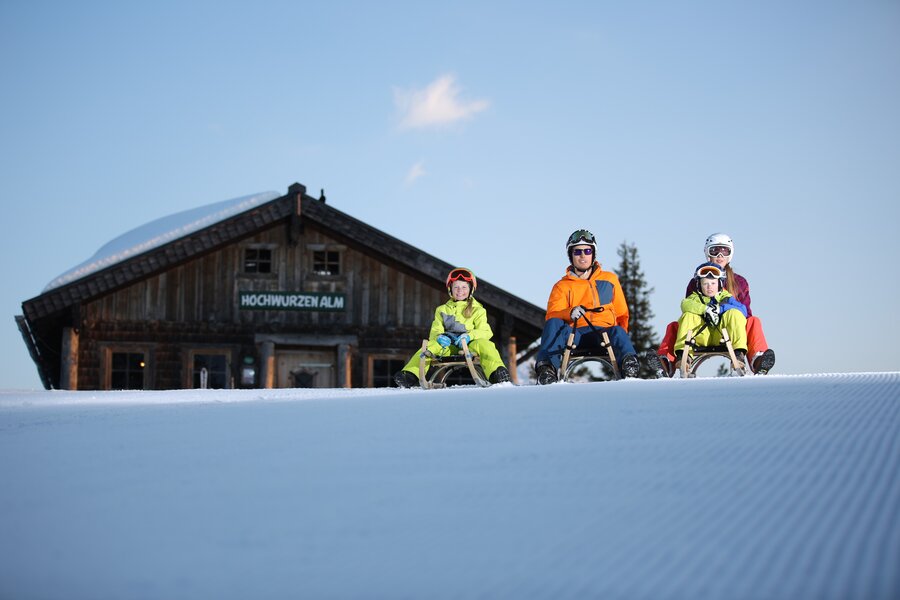 Familie rodeln auf verschneiter Piste vor Hochwurzen Alm | © MagArt.GregorHartl