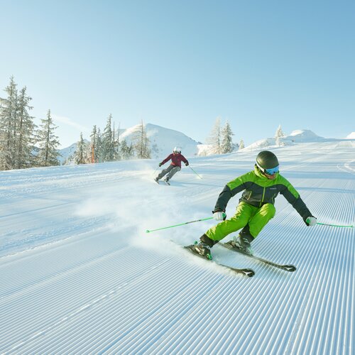 Zwei Skifahrer fahren Kurven auf einer präparierten Piste