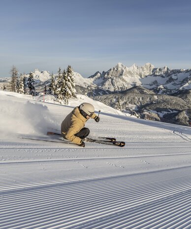 Skifahrer fährt Kurven auf präparierter Piste mit Bergkulisse | © Mirja Geh
