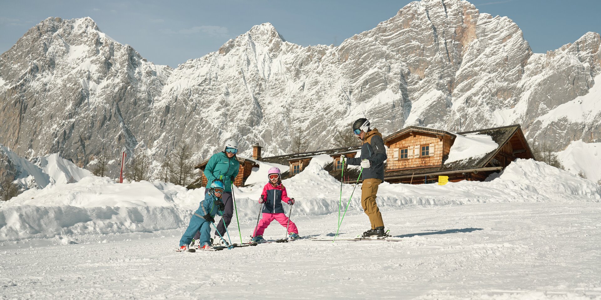 Familie beim Skifahren auf verschneiter Piste vor Bergen | © Peter Burgstaller
