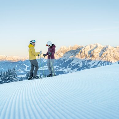 Zwei Skifahrer unterhalten sich auf verschneiter Piste mit Berglandschaft | © Peter Burgstaller