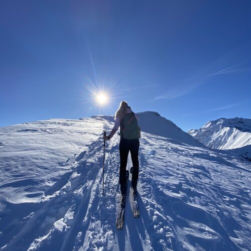Person beim Skifahren bergauf im Schnee bei Sonne