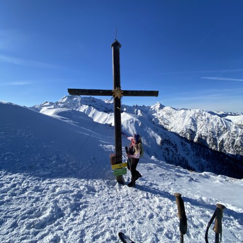 Wanderer neben einem hohen Holzkreuz am Schneegipfel, Skier im Vordergrund