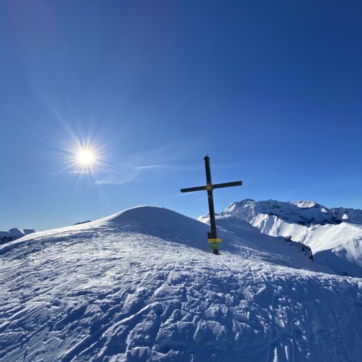 Schneebedeckter Hügel mit Holzkreuz unter blauem Himmel