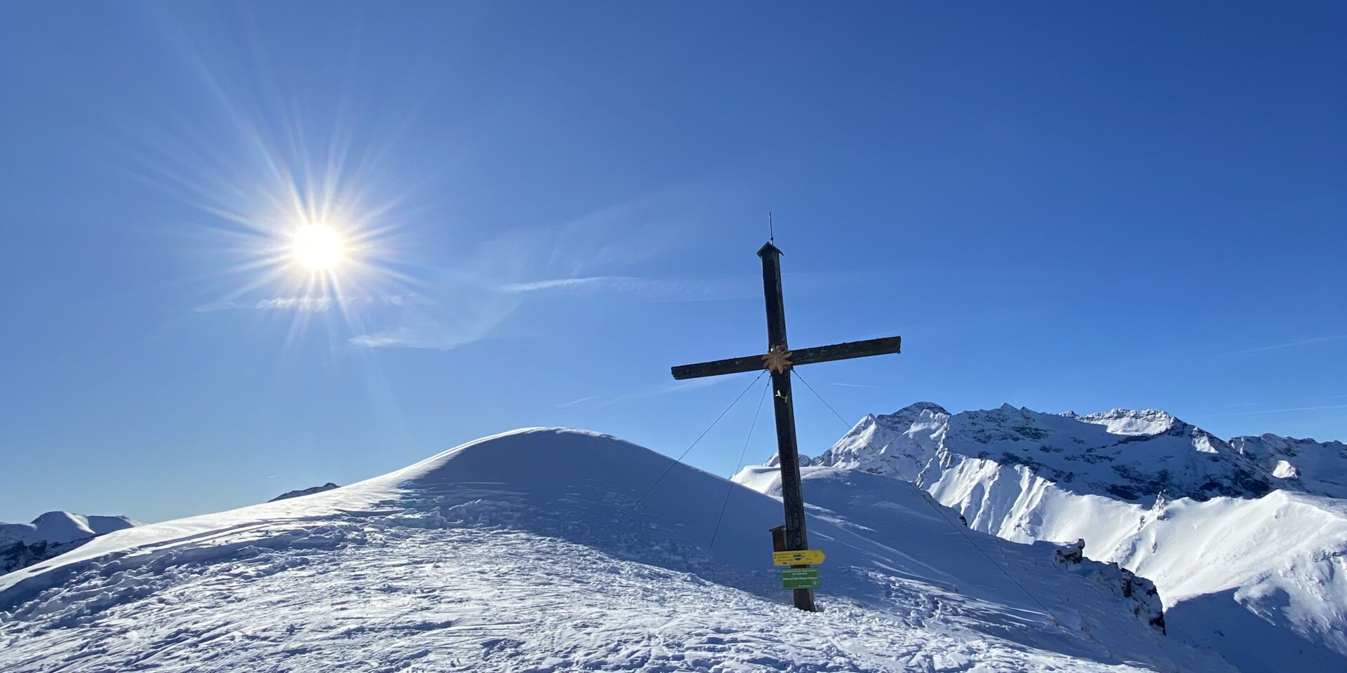 Schneebedeckter Hügel mit Holzkreuz unter blauem Himmel