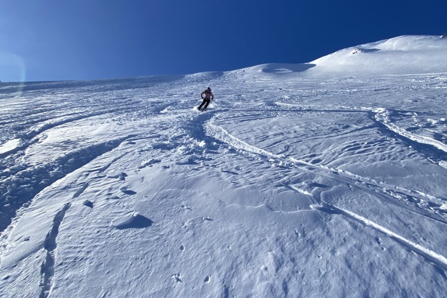 Skifahrer macht Kurven auf schneebedeckter Piste unter blauem Himmel.