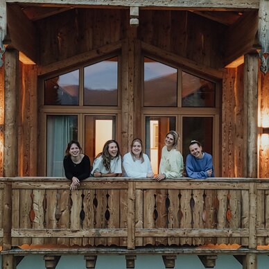 Five friends leaning on a rustic wooden cabin balcony