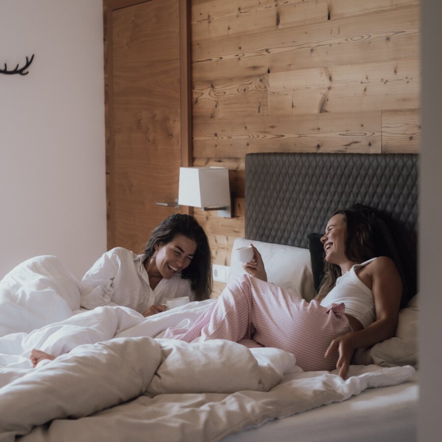 Two women laughing in bed, holding white cups