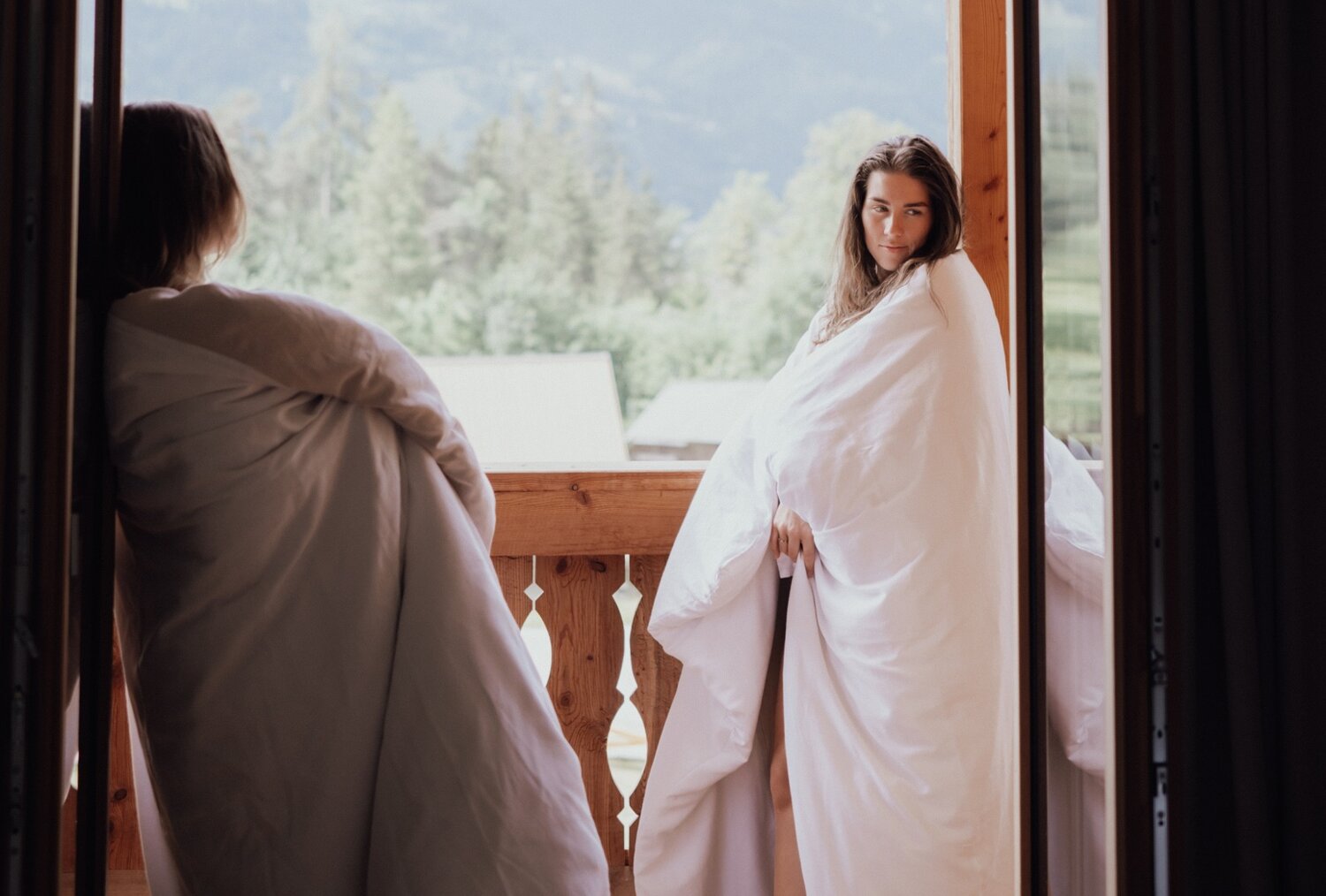 Zwei Personen in weißen Decken auf dem Balkon mit Bergblick