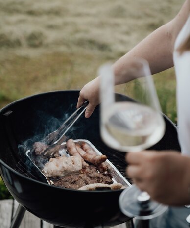 Person grillt verschiedenes Fleisch auf einem Holzkohlegrill im Freien