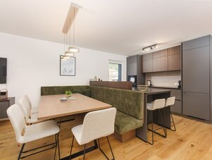 Offener Ess- und Küchenbereich mit Holztisch, grüner Bank und grauen Schränken