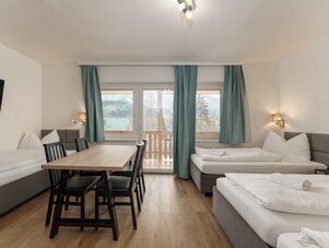 Hotelzimmer mit drei Betten, Esstisch und Bergblick