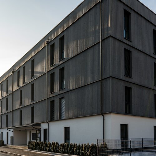 Modern four-story building with dark wooden cladding along street