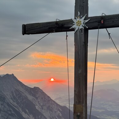 Holzkreuz mit Blüte am Berggipfel bei Sonnenuntergang