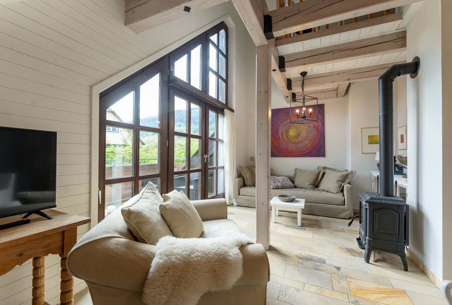 Sunlit living room with large wooden-framed windows and beams