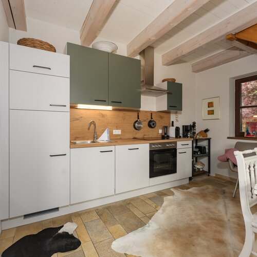 Kitchen with white and green cabinets, exposed wooden beams, and window