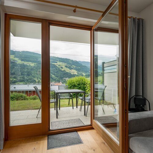 Wohnzimmer mit Glastür in Holzrahmen zum Balkon und Hügelblick
