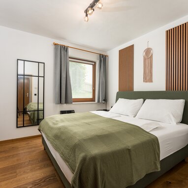 Doppelbett mit grünem gepolstertem Kopfteil und weißen Kissen im modernen Schlafzimmer.