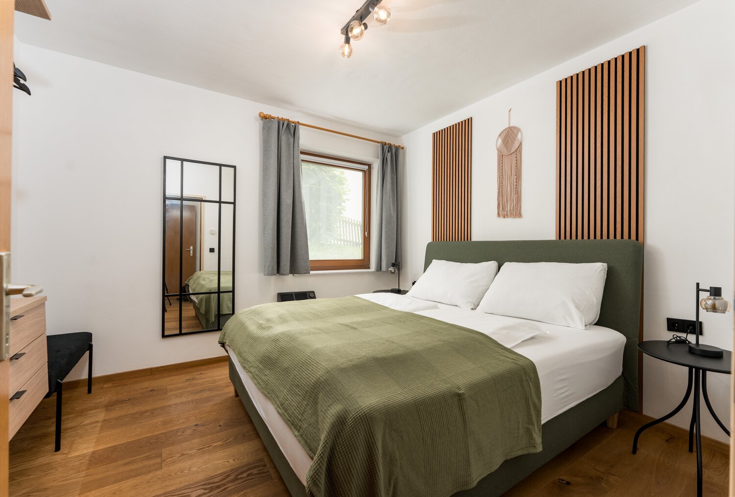 Doppelbett mit grünem gepolstertem Kopfteil und weißen Kissen im modernen Schlafzimmer.