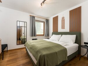 Schlafzimmer mit grünem gepolstertem Bett, Holzlattenwänden und Spiegel