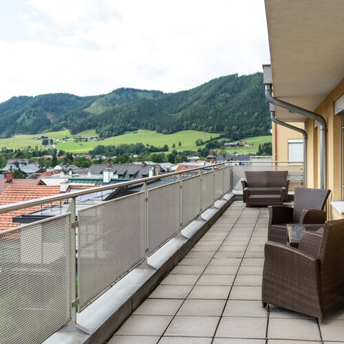 Balkon mit braunen Rattan-Sesseln, Blick auf Dorf und Berge
