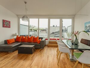 Heller offener Wohnbereich mit grauem Sofa und orangen Kissen