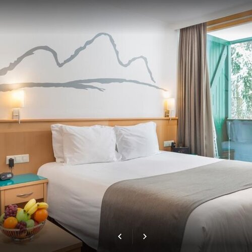 Hotelzimmer mit großem Bett, Wandbild und Balkonblick.