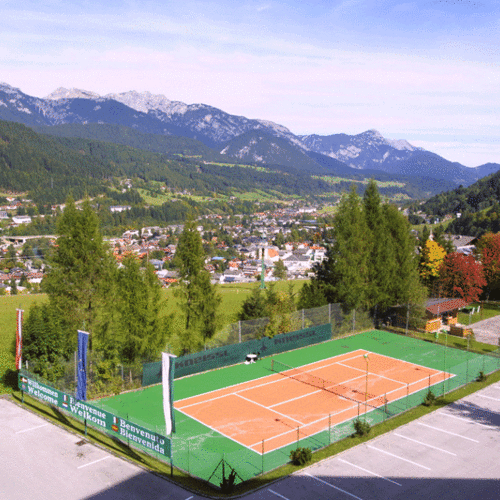 Roter Sandplatz im Alpen-Tal, Berge und Stadt im Hintergrund