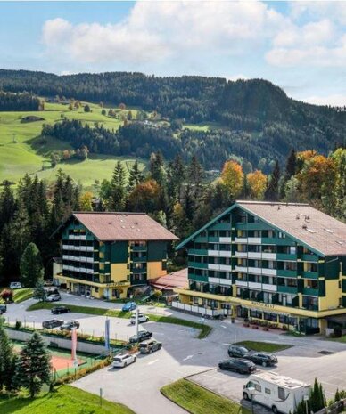 Zwei grüne Apartmenthäuser am Hang in einer Waldlandschaft | © Sarah Kurre