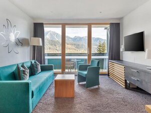Wohnzimmer mit türkisfarbenem Sofa, Stühlen und Bergblick. | © Sarah Kurre