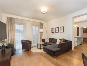 Wohnzimmer mit dunkler Eckcouch, Sessel und großen Fenstern