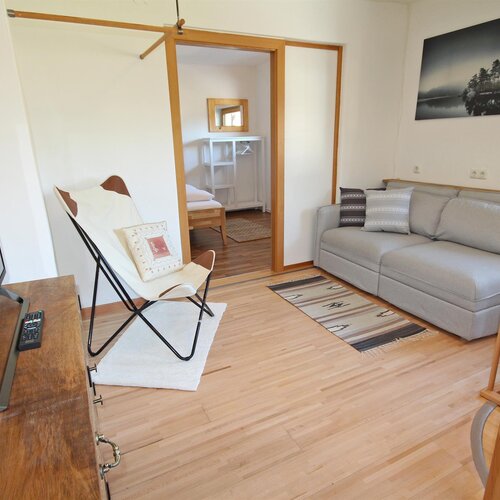 Helles Wohnzimmer mit grauer Couch, Fernseher und Stuhl