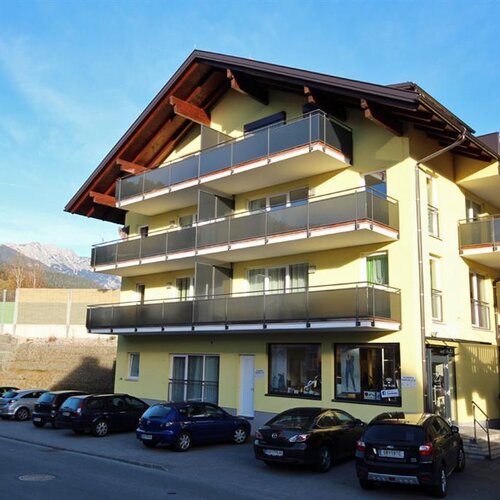 Gelbes Mehrfamilienhaus mit Balkonen und geparkten Autos