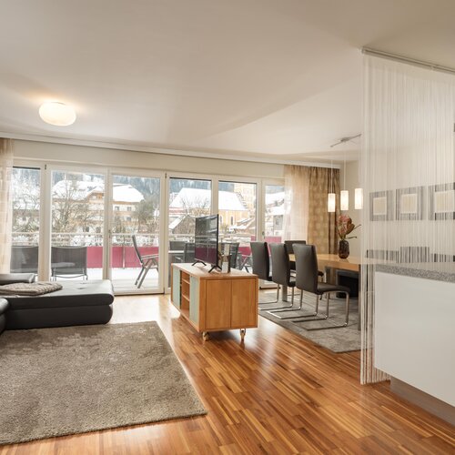 Bright open-plan living room with sofa, dining area, and balcony doors