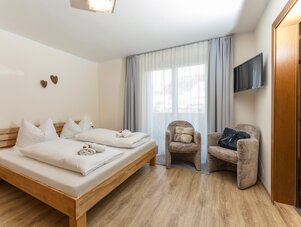 Wooden bed with white bedding and two armchairs by window