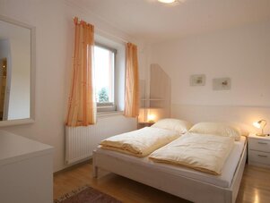 Helles Schlafzimmer mit Doppelbett, Nachttischen, Fenster und Vorhängen