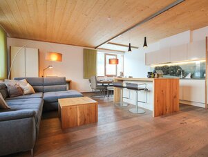 Open-plan living area with blue sofa, wooden ceiling and kitchen island | © SCHLADMING-APPARTEMENTS