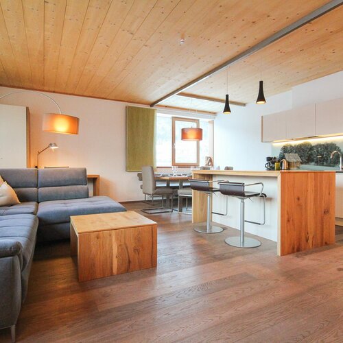 Offener Wohnbereich mit blauem Sofa, Holzdecke und Kücheninsel | © SCHLADMING-APPARTEMENTS