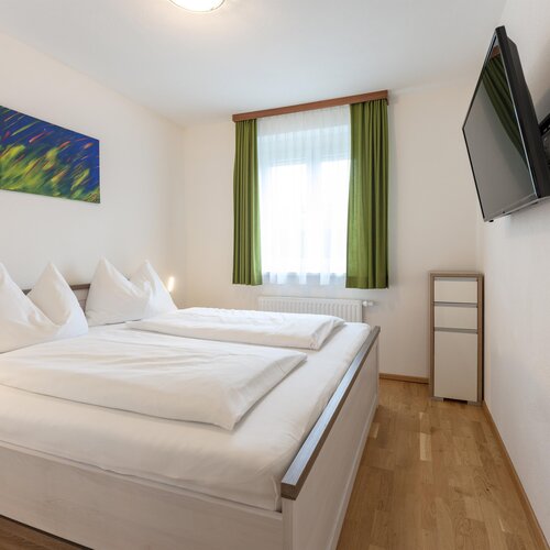 Helles Hotelzimmer mit weißer Bettwäsche und grünen Vorhängen