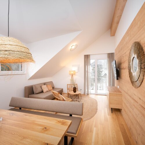 Gemütliches Wohnzimmer mit Holzverkleidung, beigem Sofa und geflochtenen Hängelampen