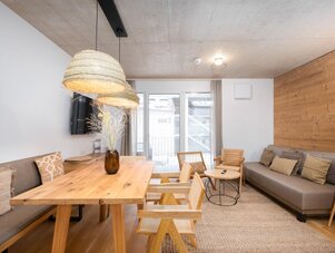 Helles Wohnzimmer mit massivem Holztisch und Sofa, Zugang zum Balkon durch Schiebetür