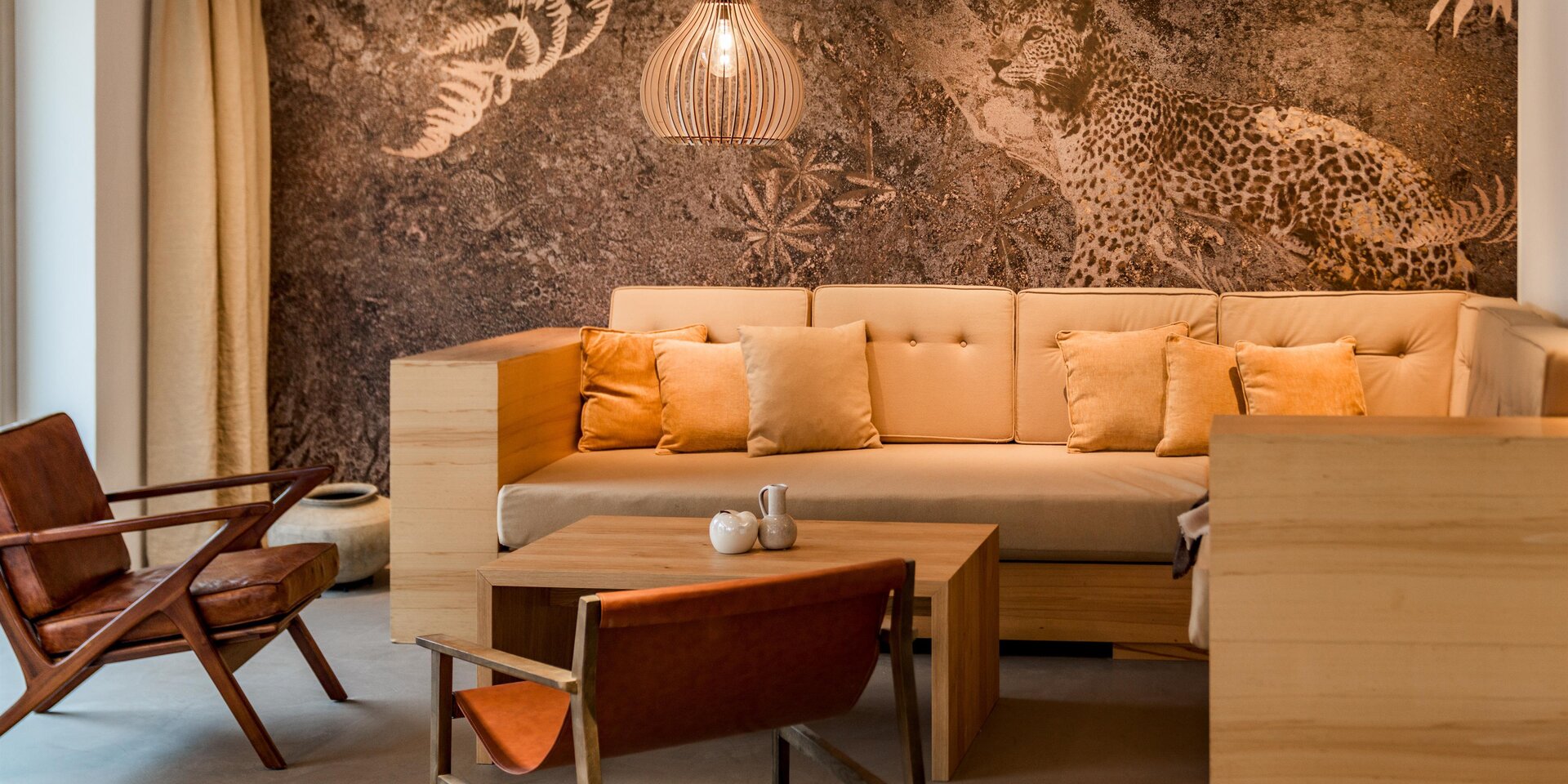 Gemütliche Lounge mit beigem Sofa, Holzmöbeln und Dschungel-Wandbild.