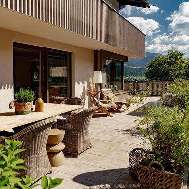 Terrasse mit Holztisch, Korbstühlen und Topfpflanzen