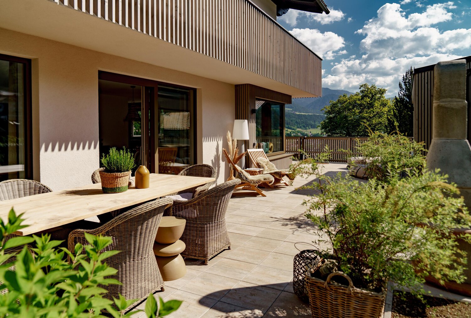 Terrasse mit Holztisch, Korbstühlen und Topfpflanzen