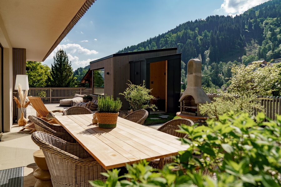 Sonnenbeschienene Terrasse mit Holztisch, Korbstühlen und Pflanzen