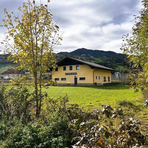 Foreground trees frame a yellow house in a hilly landscape