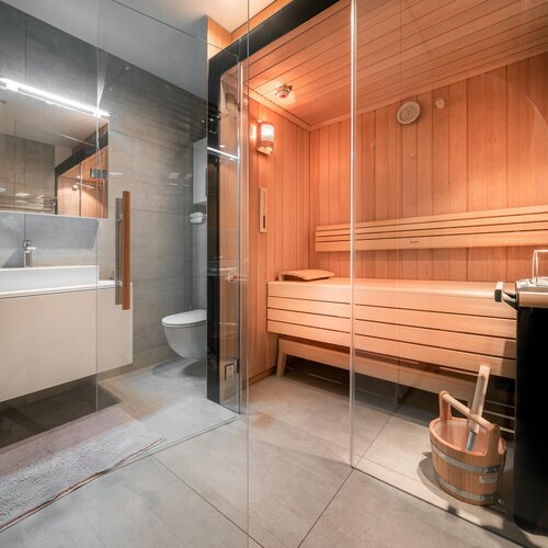 Modernes Badezimmer mit Glaswand trennt Dusche und Holzsauna.