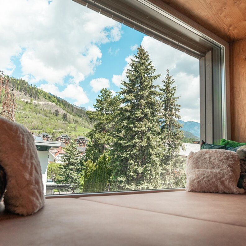 Cozy window seat indoors with mountains and trees outside.