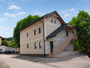 Two-story beige building with an outdoor wooden staircase beside trees